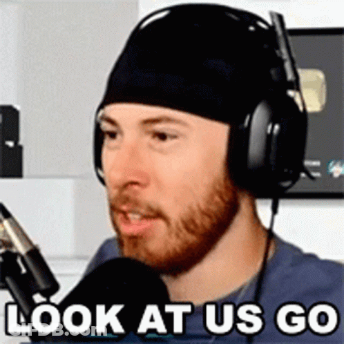 A Man Wearing Headphones And A Beanie Is Talking Into A Microphone And Says `` Look At Us Go '' . GIF