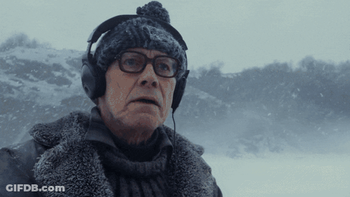 A Man Wearing Headphones And A Beanie Looks At The Camera In The Snow GIF