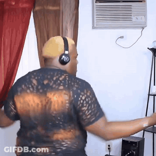 A Man Wearing Headphones And A Black Shirt Is Dancing In A Living Room GIF