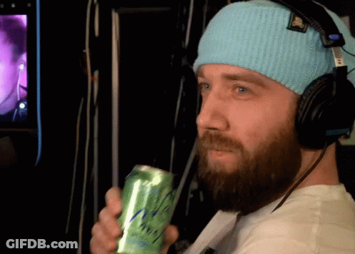 A Man Wearing Headphones And A Blue Beanie Holds A Green Can GIF