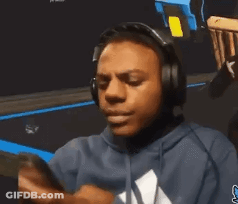 A Man Wearing Headphones And A Blue Hoodie Is Looking At His Cell Phone . GIF