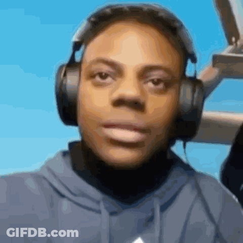 A Man Wearing Headphones And A Blue Hoodie Is Looking At The Camera . GIF