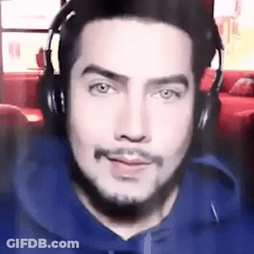 A Man Wearing Headphones And A Blue Hoodie Is Smiling . GIF