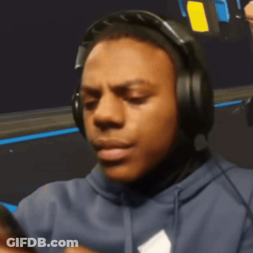 A Man Wearing Headphones And A Blue Hoodie Looks At His Phone GIF