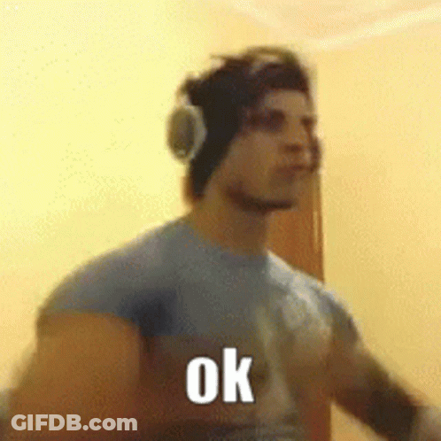 A Man Wearing Headphones And A Blue Shirt Is Standing In Front Of A Wall And Says Ok . GIF