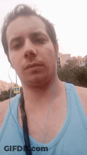 A Man Wearing Headphones And A Blue Tank Top Is Standing In Front Of A Crosswalk Sign GIF