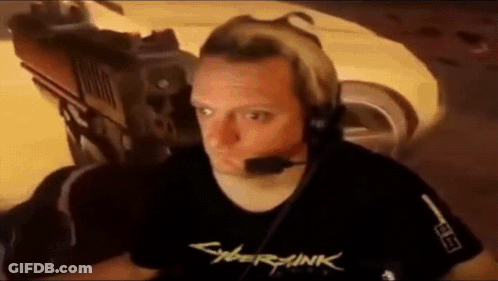 A Man Wearing Headphones And A Cyberpunk 2077 T-Shirt Is Sitting In Front Of A Car . GIF