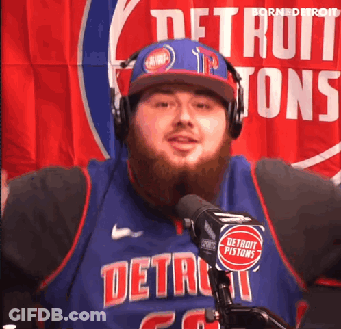 A Man Wearing Headphones And A Detroit Pistons Jersey Stands In Front Of A Microphone GIF