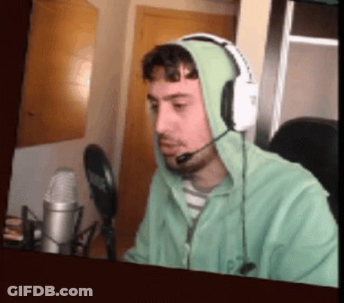 A Man Wearing Headphones And A Green Hoodie Is Talking Into A Microphone . GIF