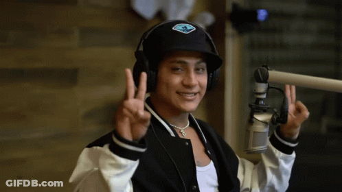 A Man Wearing Headphones And A Hat Giving The Peace Sign GIF