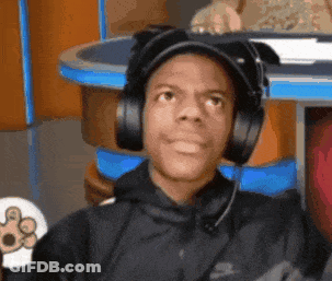A Man Wearing Headphones And A Hat Is Sitting At A Table GIF