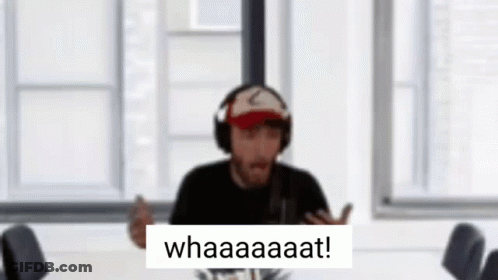 A Man Wearing Headphones And A Hat Is Sitting At A Table With A Sign That Says Whaaaaaat . GIF