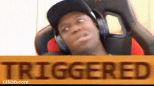 A Man Wearing Headphones And A Hat Is Sitting In A Chair Behind A Sign That Says `` Triggered '' . GIF