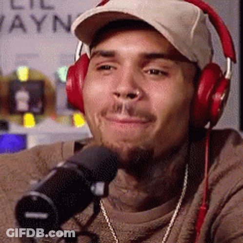 A Man Wearing Headphones And A Hat Is Sitting In Front Of A Microphone . GIF
