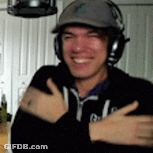 A Man Wearing Headphones And A Hat Is Smiling . GIF