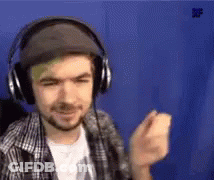 A Man Wearing Headphones And A Hat Is Standing In Front Of A Blue Wall . GIF