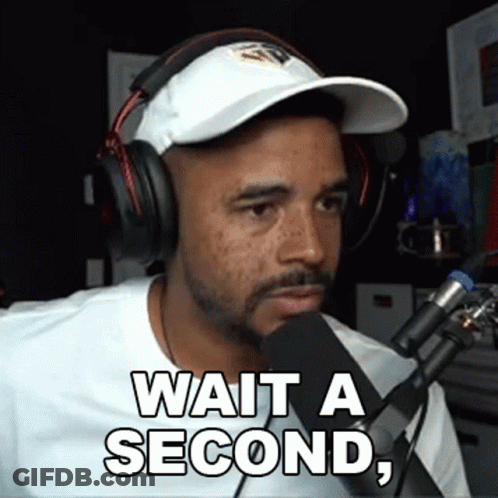 A Man Wearing Headphones And A Hat Is Talking Into A Microphone And Says Wait A Second GIF