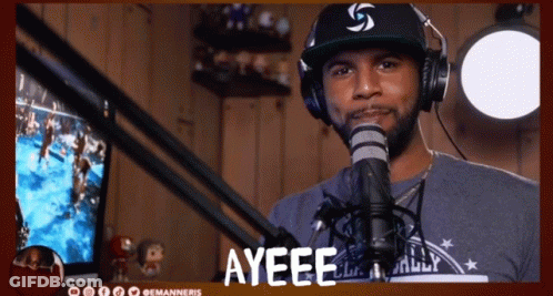 A Man Wearing Headphones And A Hat Stands In Front Of A Microphone With The Word Ayeee Above Him GIF