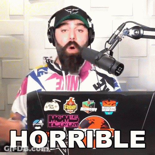 A Man Wearing Headphones And A Hat Stands In Front Of A Microphone With The Word Horrible Written Below Him GIF