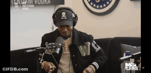 A Man Wearing Headphones And A Hat With A Skull And Crossbones On It Talks Into A Microphone GIF