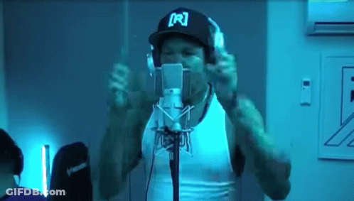 A Man Wearing Headphones And A Hat With The Letter R On It Is Singing Into A Microphone GIF