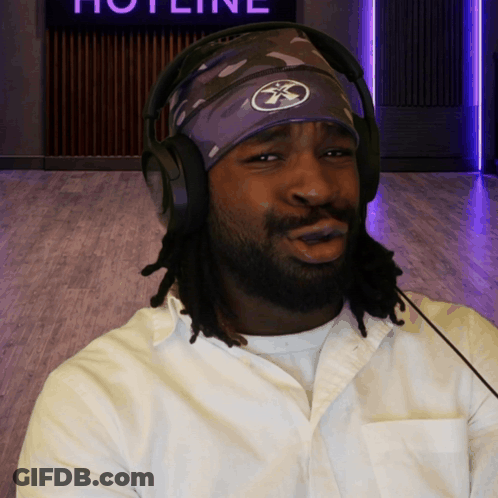 A Man Wearing Headphones And A Headband With The Word Hotline On The Wall Behind Him GIF