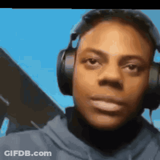 A Man Wearing Headphones And A Hoodie Is Looking At The Camera . GIF