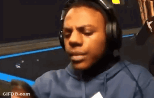 A Man Wearing Headphones And A Hoodie Looks At His Phone GIF
