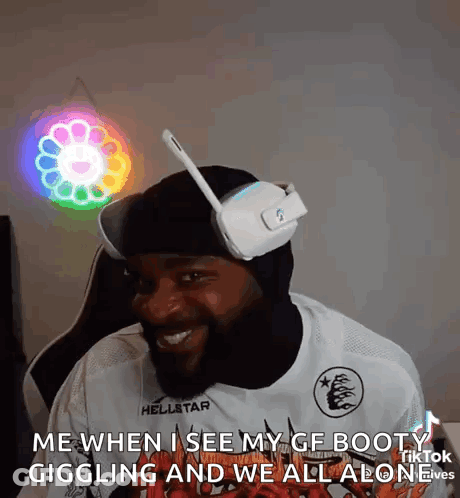 A Man Wearing Headphones And A Mask Is Sitting In Front Of A Neon Flower . GIF