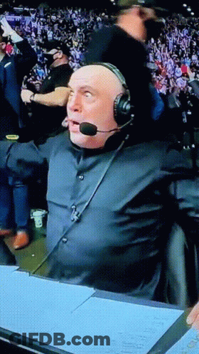 A Man Wearing Headphones And A Microphone Is Sitting In Front Of A Crowd GIF