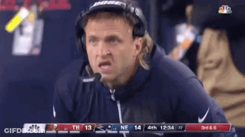 A Man Wearing Headphones And A Microphone Is Sitting On The Sidelines During A Football Game . GIF