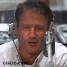 A Man Wearing Headphones And A Microphone Is Talking Into A Microphone . GIF