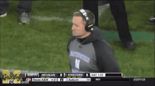 A Man Wearing Headphones And A Northwestern Shirt Watches A Football Game GIF