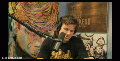 A Man Wearing Headphones And A Paid T-Shirt Is Sitting In Front Of A Microphone GIF