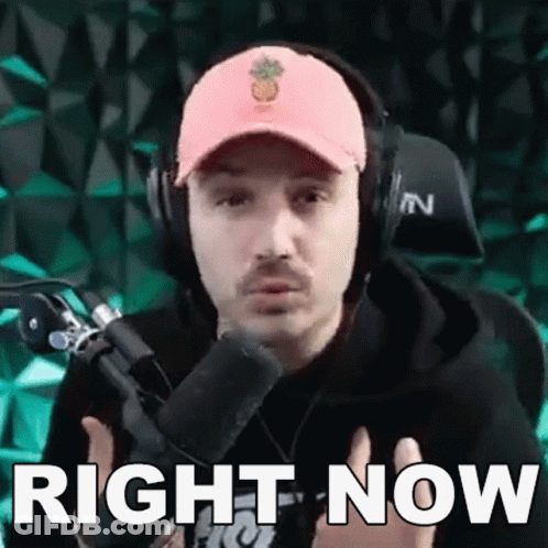 A Man Wearing Headphones And A Pink Hat Is Standing In Front Of A Microphone And Says `` Right Now '' . GIF