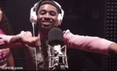 A Man Wearing Headphones And A Pink Shirt Is Standing In Front Of A Microphone GIF