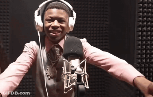 A Man Wearing Headphones And A Pink Shirt Is Standing In Front Of A Microphone GIF