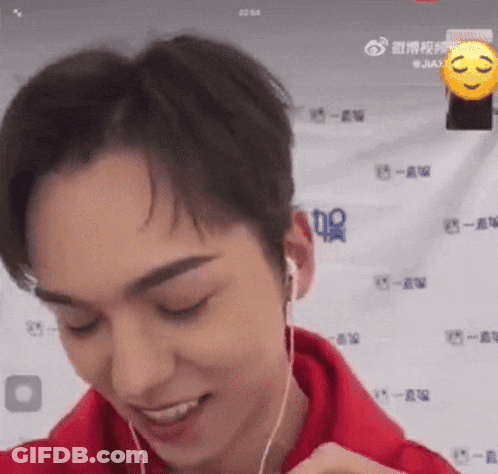 A Man Wearing Headphones And A Red Hoodie Is Smiling And Looking At The Camera . GIF