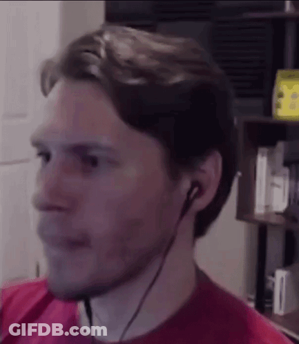 A Man Wearing Headphones And A Red Shirt Is Looking At The Camera . GIF