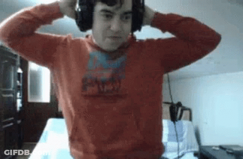 A Man Wearing Headphones And A Red Sweater Is Standing In A Room . GIF