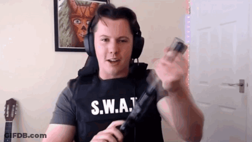 A Man Wearing Headphones And A S.w.a.t Vest Is Holding A Gun In His Hand . GIF