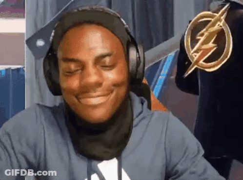 A Man Wearing Headphones And A Scarf Is Smiling And Looking At The Camera . GIF