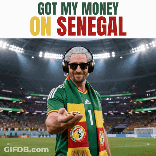 A Man Wearing Headphones And A Scarf With The Number 1 On It Holds A Coin In Front Of A Soccer Field GIF