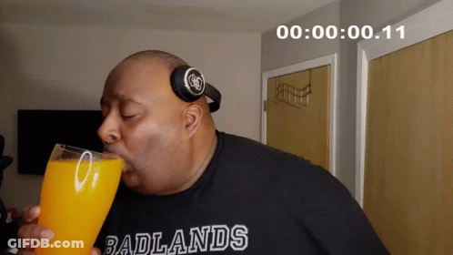 A Man Wearing Headphones And A Shirt That Says Badlands Drinks A Glass Of Orange Juice GIF