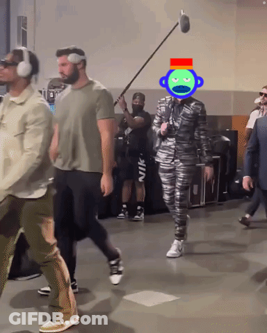 A Man Wearing Headphones And A Suit Has A Green Monkey On His Head GIF