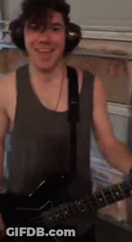 A Man Wearing Headphones And A Tank Top Is Holding A Guitar GIF