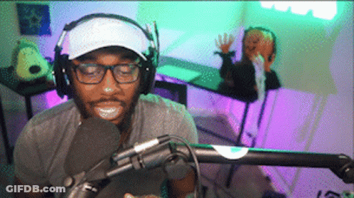A Man Wearing Headphones And A White Hat Is Talking Into A Microphone GIF