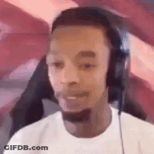 A Man Wearing Headphones And A White Shirt Is Sitting In Front Of A Computer Screen . GIF