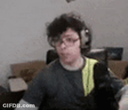 A Man Wearing Headphones And Glasses Is Sitting In A Living Room With A Cat . GIF