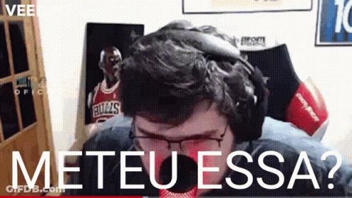 A Man Wearing Headphones And Glasses Is Sitting In Front Of A Bulls Poster .. GIF